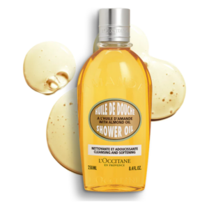 Flasche Duschöl mit Mandelöl, umgeben von zwei Tropfen des Produkts auf einem hellen Hintergrund.