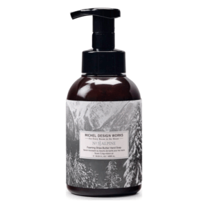 Braune Pumpflasche mit schäumender Shea-Butter-Handseife, dekoriert mit schneebedecktem Bergmotiv.