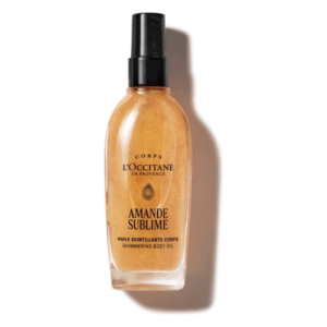 Transparente Flasche mit schimmerndem Körperöl von L'Occitane, goldene Flüssigkeit, schwarzer Sprühkopf.