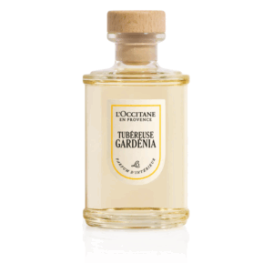 Ein transparenter Glasbehälter mit holzfarbenem Verschluss, gefüllt mit einem Duft namens Tubéreuse Gardenia von L'Occitane.